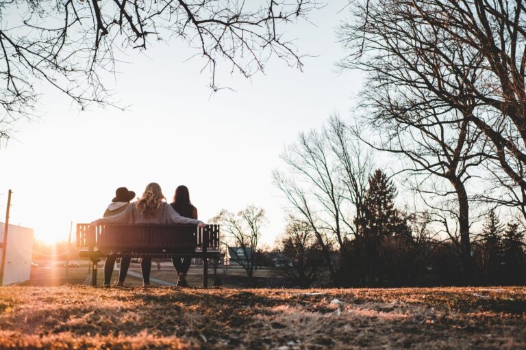 Three women sitting on a park bench in a fall landscape