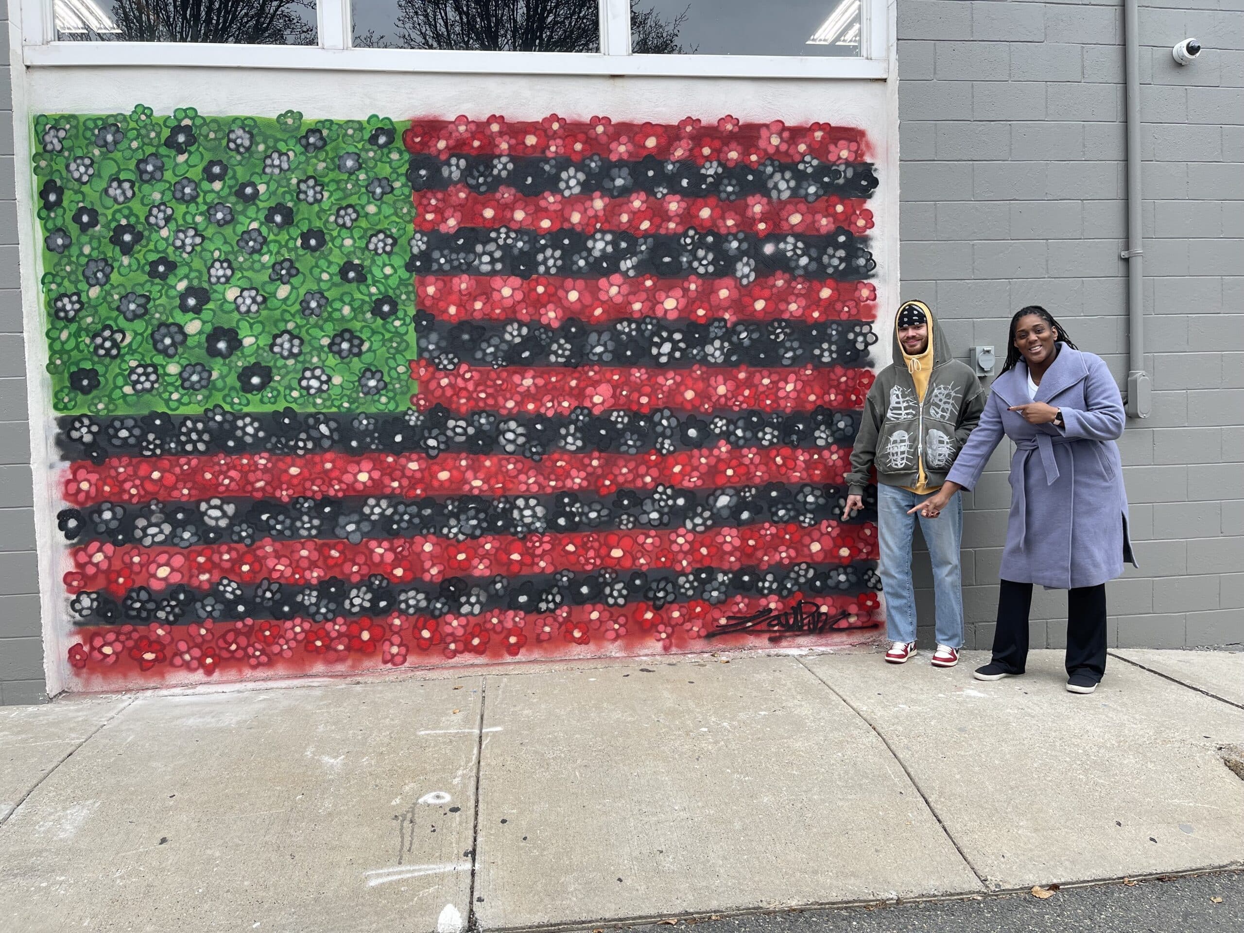 Mural Arist, Jordan Carter (left), and The Heritage Club Founder, Nike John (right), point to Jordan's mural - David Hammons’ African American Flag.